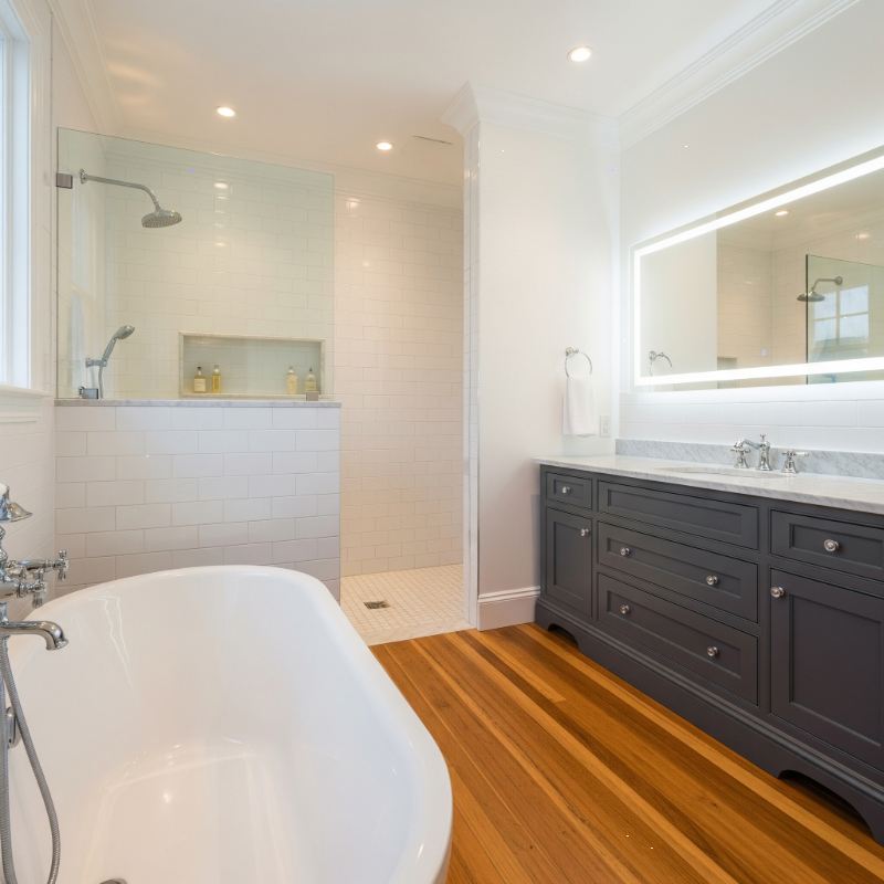Contemporary bathroom interior in Kolkata with bathtub, wooden floor, LED mirror, and glass shower